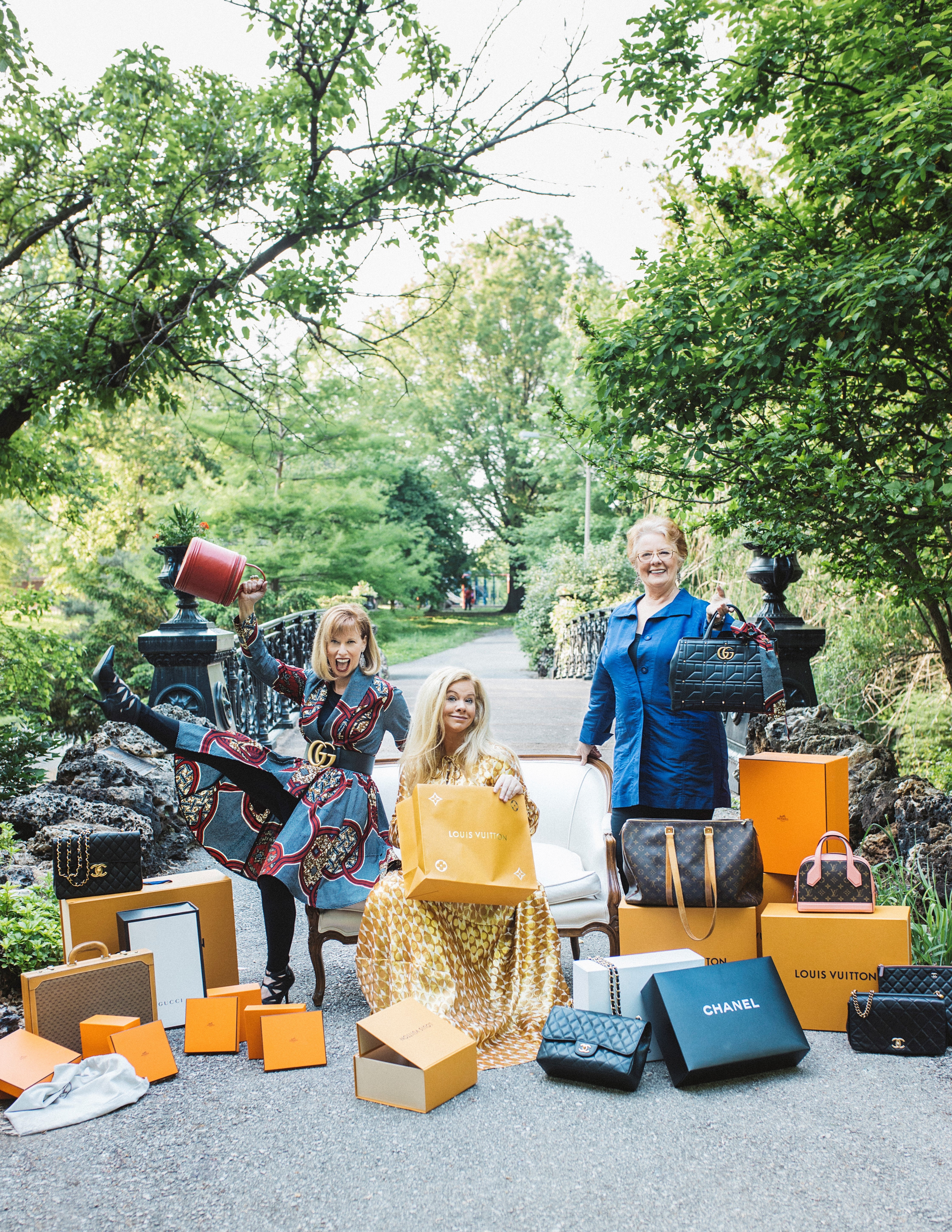 A photograph of Diana, Laura, and Sue in Forest Park, surrounded by Louis Vuitton and Chanel handbags and boxes.