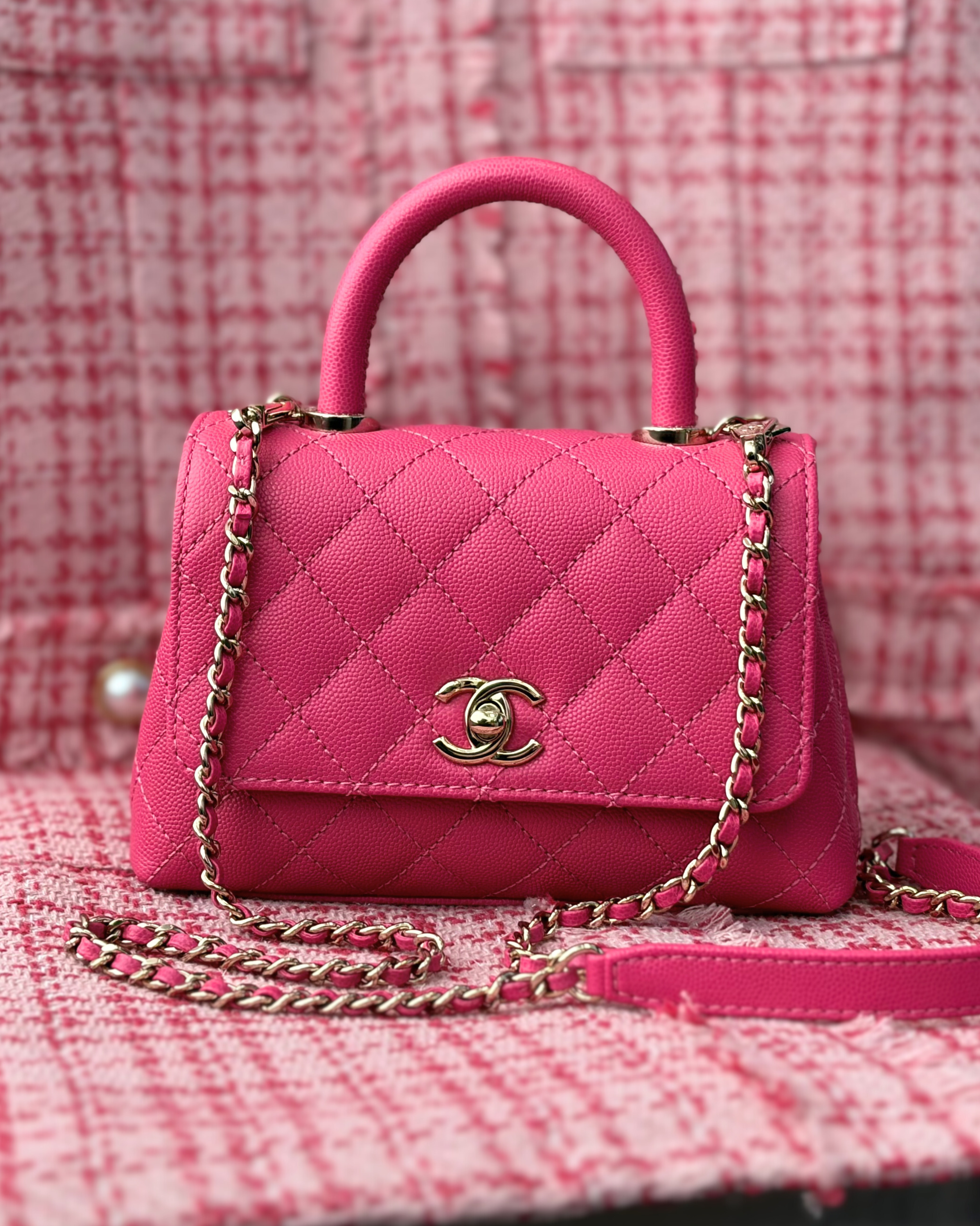 A pink Chanel handbag on a pink tweed background.