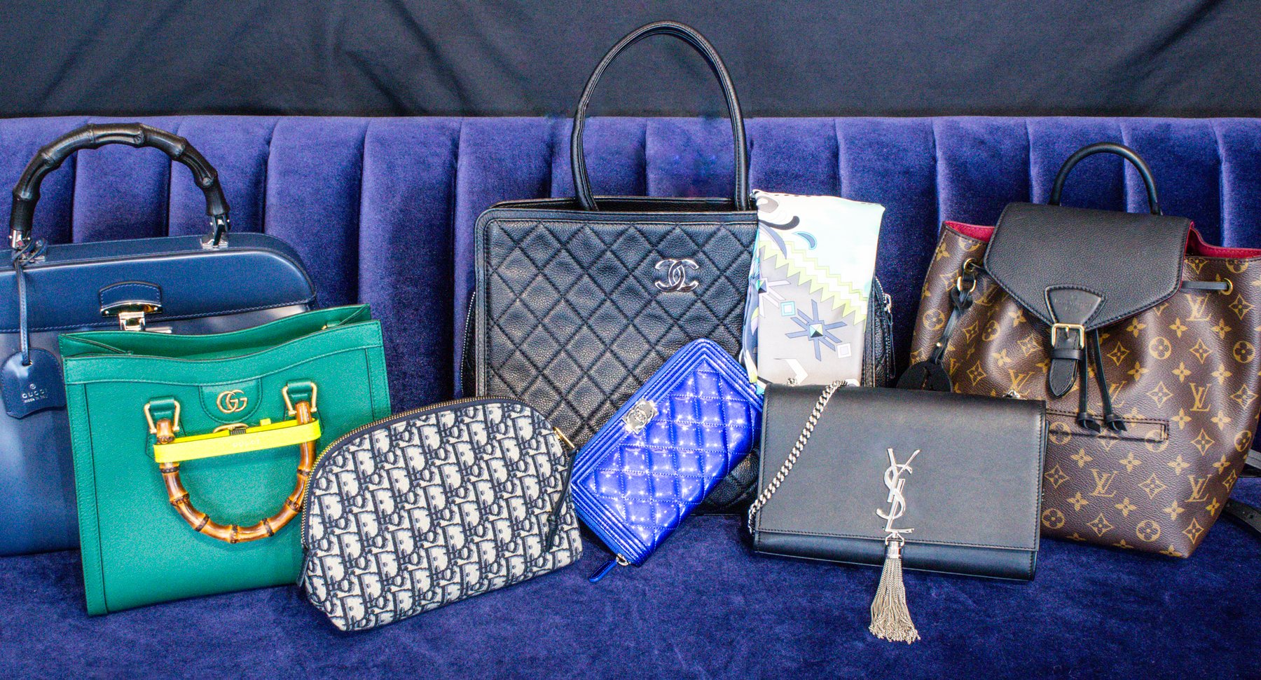 A collection of luxury handbags available to purchase from The Vault Luxury Resale, organized on a couch. The bags are Gucci, Dior, Chanel, Saint Laurent, and Louis Vuitton.