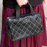 Black quilted handbag with top handles, gold lattice stitching, and CHANEL logo