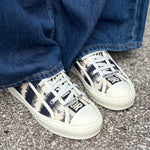 DIOR D-stripe sneakers in black-and-cream canvas with white laces, worn with cuffed jeans