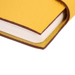 Yellow notebook cover corner detail with stitched edge and visible page edges