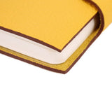 Yellow notebook cover corner detail with stitched edge and visible page edges