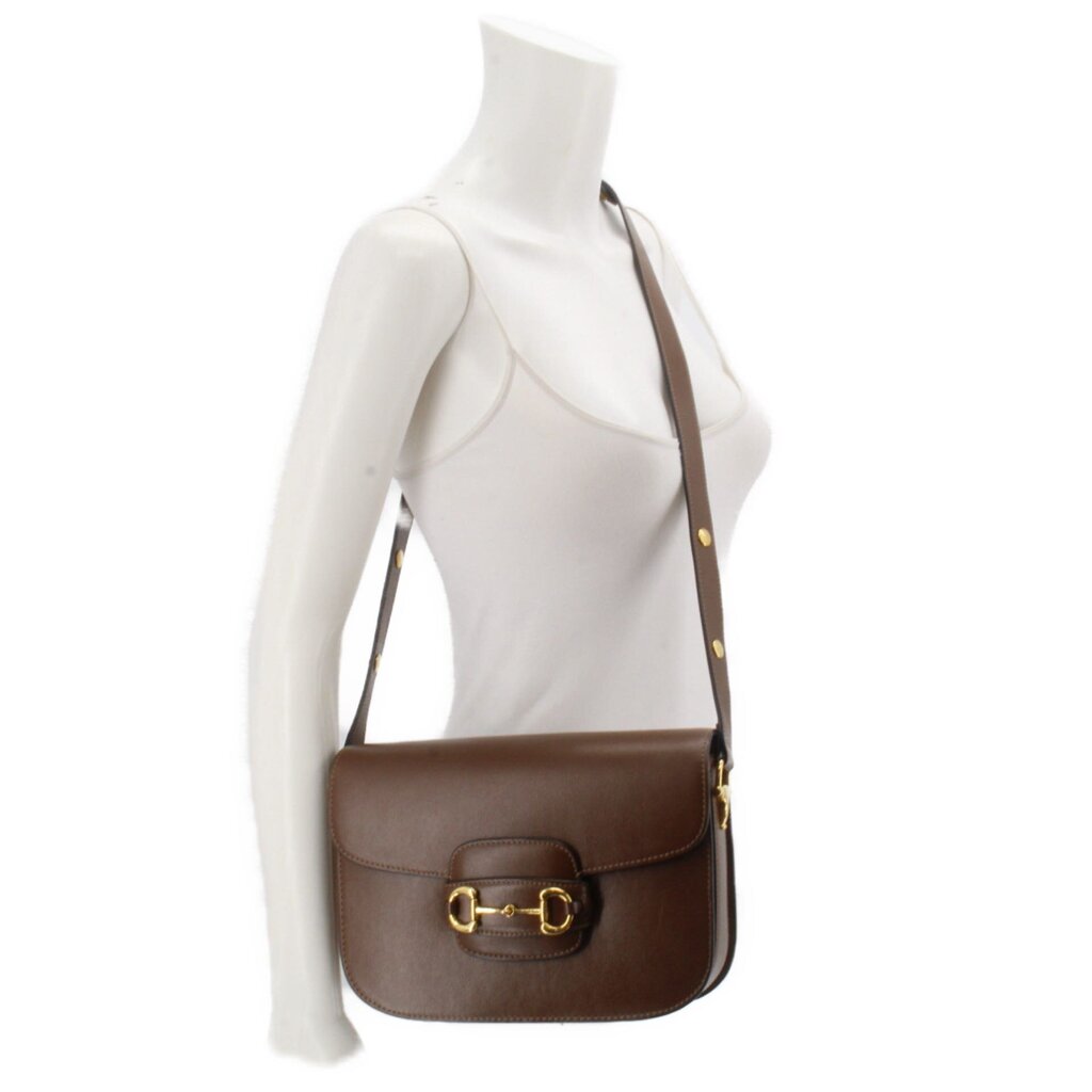 Brown leather shoulder bag worn crossbody with gold Horsebit clasp.