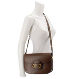 Brown leather shoulder bag worn crossbody with gold Horsebit clasp.