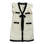 White and black button-up dress with ruffled sleeves, patch pockets, and black bow tie