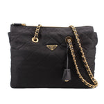 Black quilted tote bag with gold chain strap, top zip, and Prada logo plaque