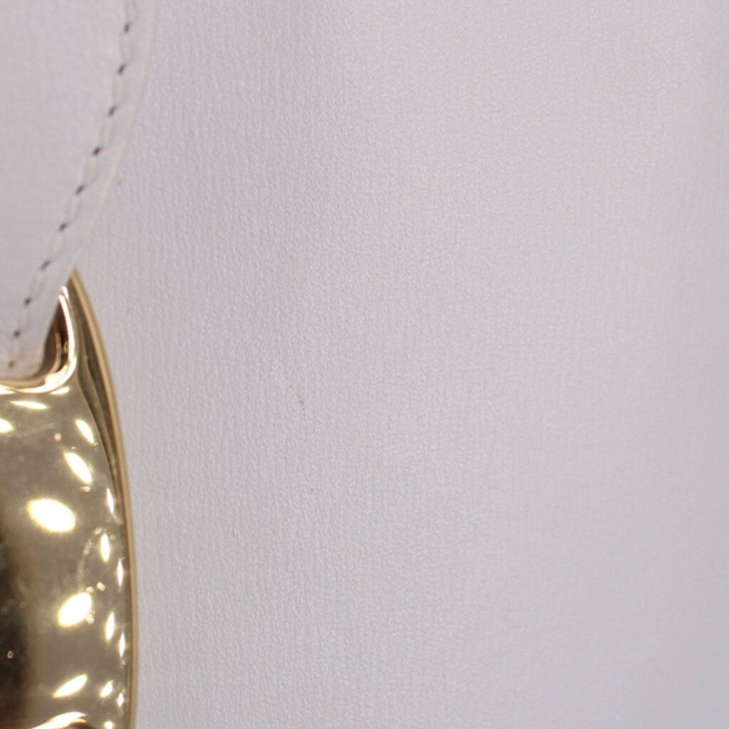 Close-up of white leather crossbody tote edge with metallic logo snap