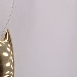 Close-up of white leather crossbody tote edge with metallic logo snap