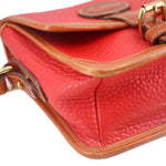 Close-up of red crossbody corner with tan trim, curved seam, and gold hardware details