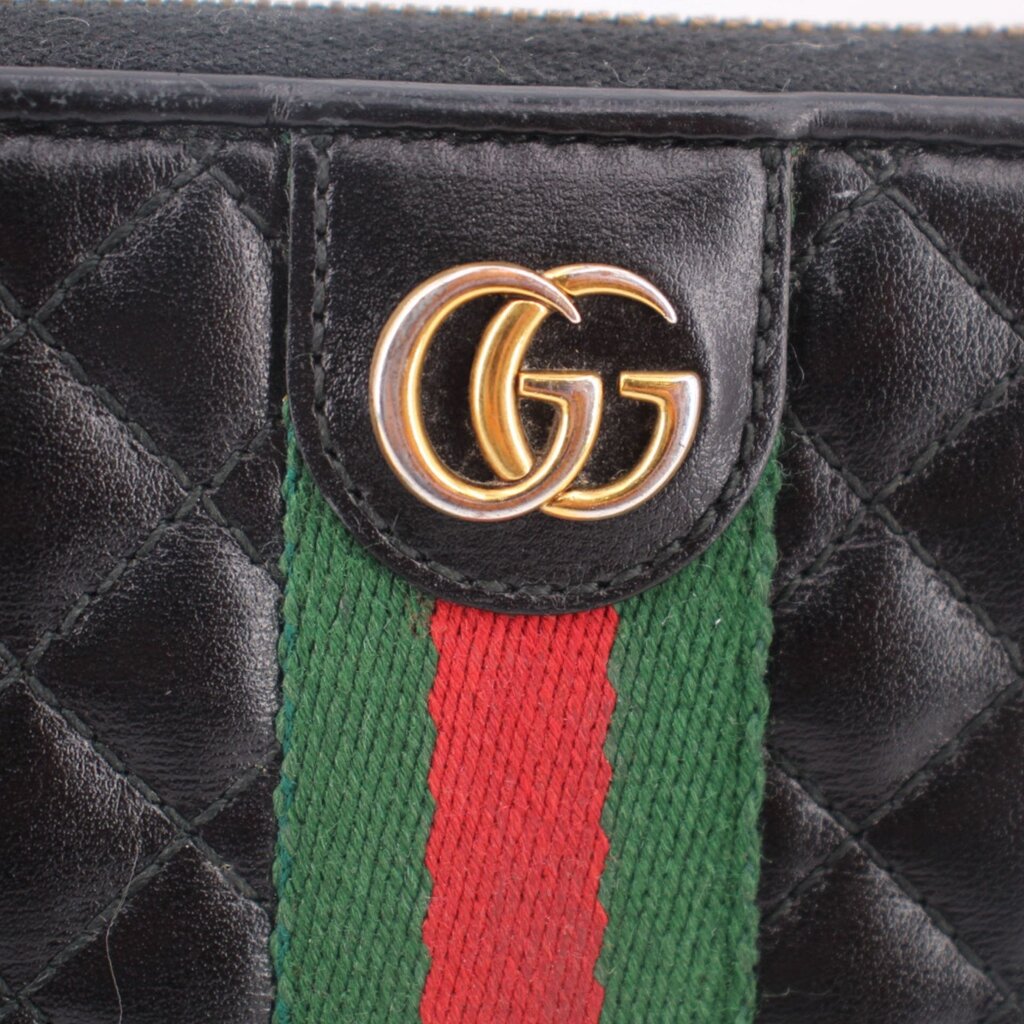 GG logo plaque on black quilted leather with green and red Web stripe, close-up.