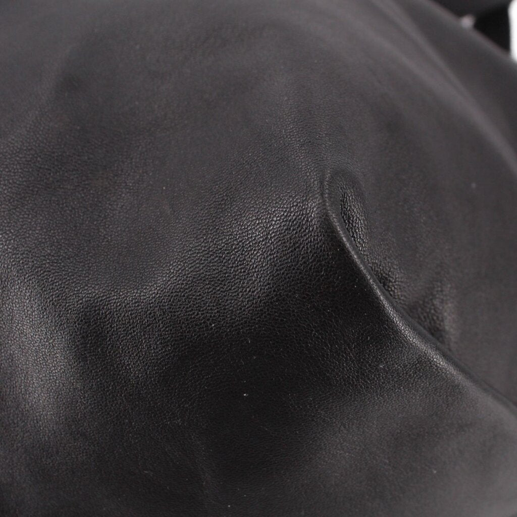 Close-up of black drawstring tote bag leather panels and subtle creasing near seam.