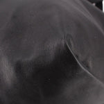 Close-up of black drawstring tote bag leather panels and subtle creasing near seam.