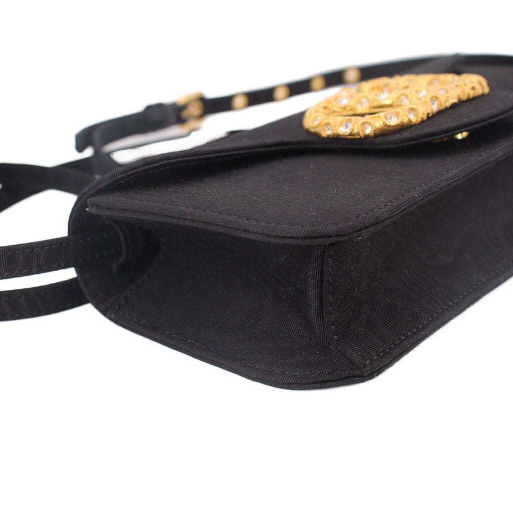Black crossbody bag close-up with gold-tone logo emblem and stitched flap edge