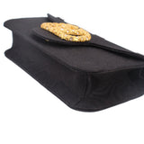 Black crossbody bag corner view with gold-tone logo emblem and textured fabric panel