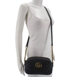 Black leather camera crossbody bag worn with gold-tone chain strap and GG logo front.