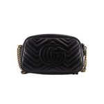 Black quilted camera crossbody bag with raised GG logo pattern and gold-tone hardware.