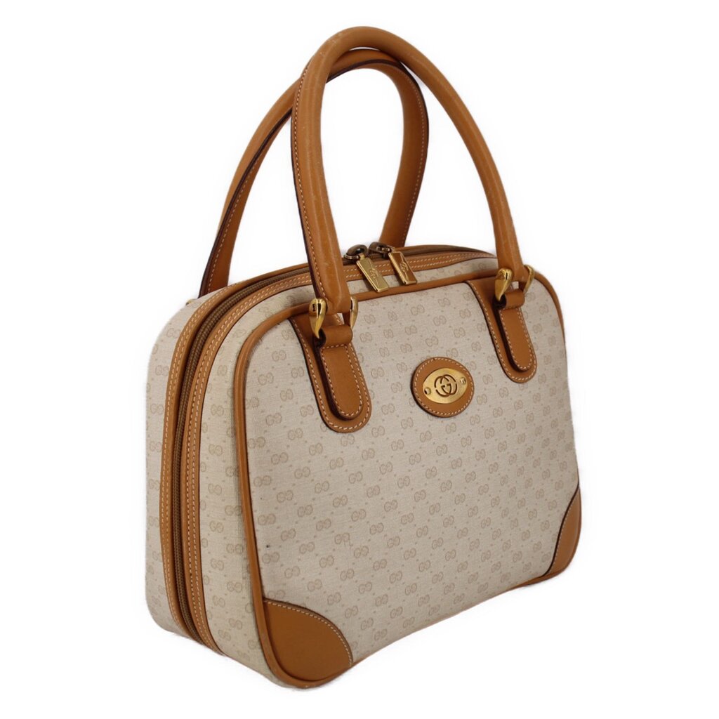 Beige canvas tote-style handle bag with tan leather strap and circular front logo patch