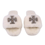 Cream shearling slide slippers showing front jeweled cross emblem, pair