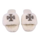 Cream shearling slide slippers showing front jeweled cross emblem, pair