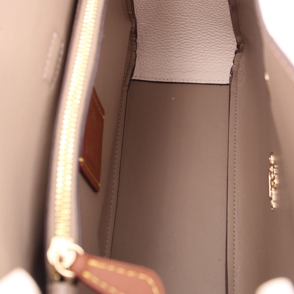 Cream crossbody interior view with zipper track and brown lining pocket, close-up.