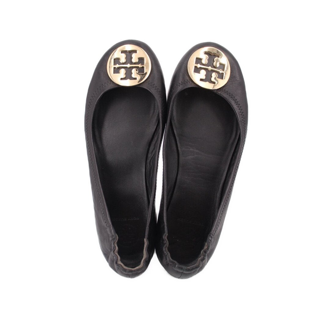 Pair of black ballet flats, top view showing gold logo medallion