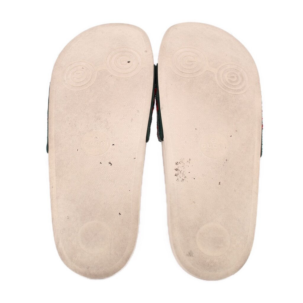 Bottom view of green velvet slide sandals with beige outsoles and circular tread marks