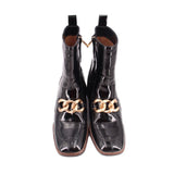 Pair of black glossy ankle boots with gold-tone chain detail and low block heel