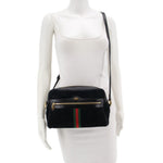 Black suede crossbody bag worn on model with adjustable strap and green-red web stripe
