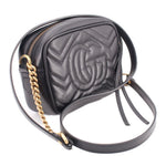 Black quilted leather crossbody bag with embossed GUCCI double-G on front and dangling tag