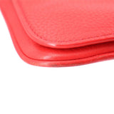 Red leather crossbody bag corner with curved trim and pebbled texture