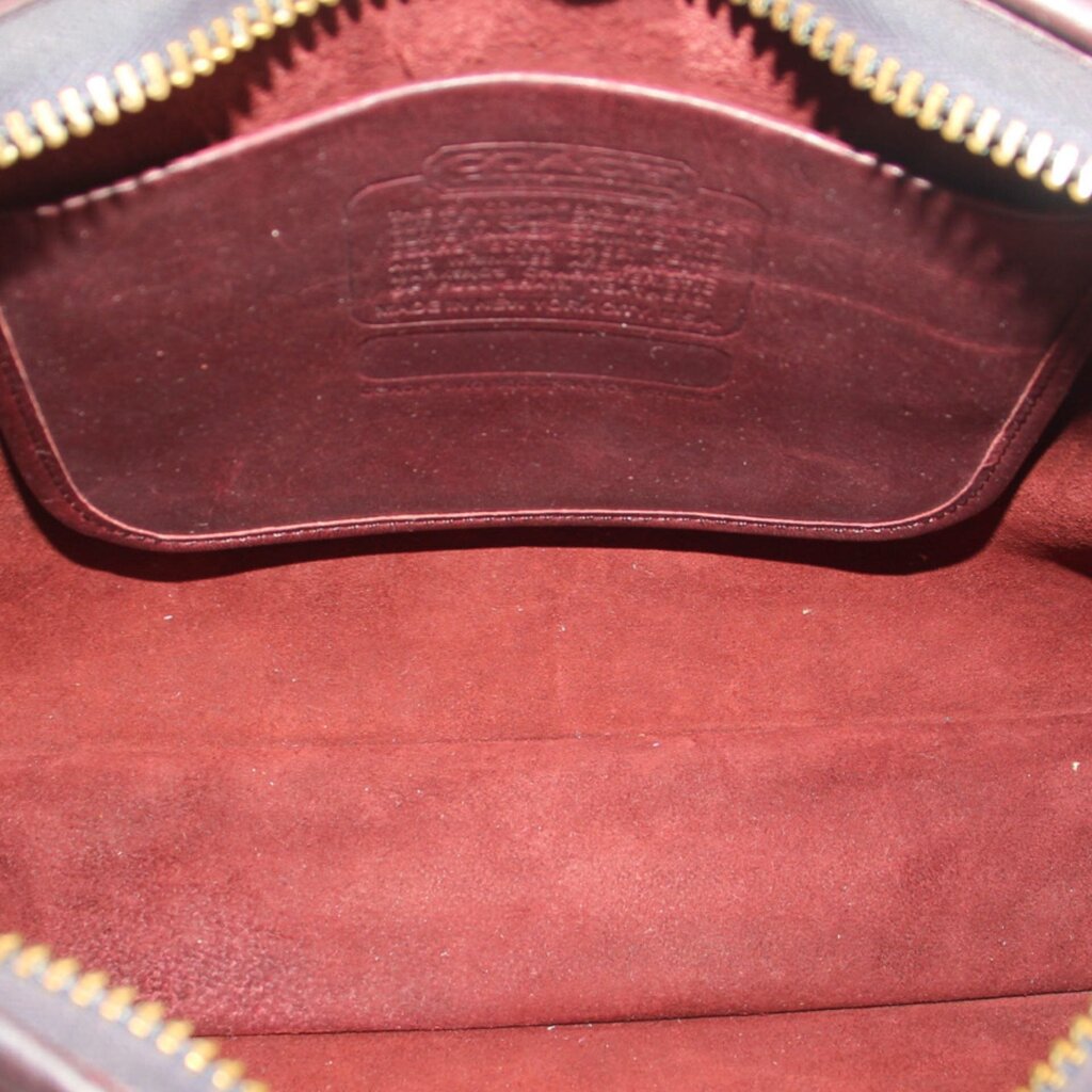 Oxblood leather satchel interior with embossed logo and gold zipper trim