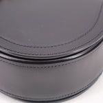 Black leather shoulder bag close-up of curved edge with contrast stitching