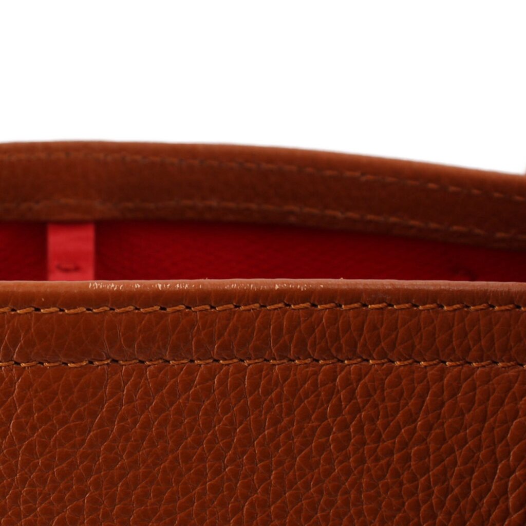 Close-up of brown tote bag seam with red interior lining and stitched edge.
