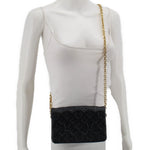 Black embossed monogram crossbody bag worn with gold chain strap