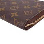 Close-up of brown monogram wallet corner with gold zipper trim and stitching.