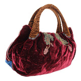 Maroon velvet mini bag with top handles and embroidered crest motifs along the front