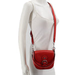Red leather crossbody bag worn across chest with adjustable strap and metal rings