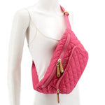 Pink quilted sling belt bag worn on model, adjustable strap and front zipper pulls
