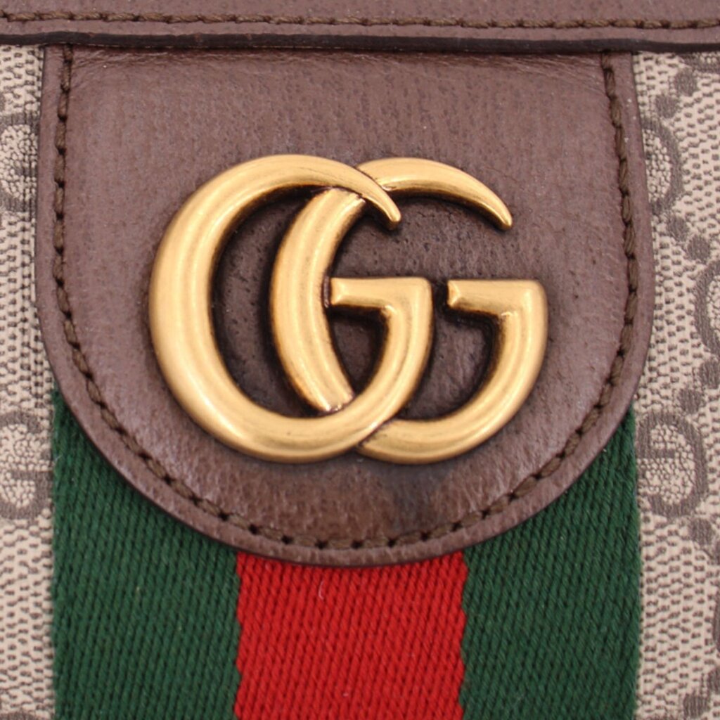 Gold GG logo plaque on brown leather pocket above green-red web stripe