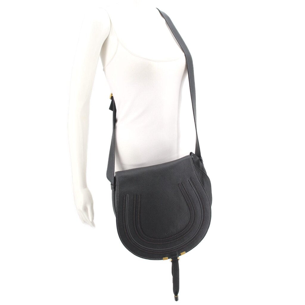 Black saddle crossbody bag worn with adjustable strap on a mannequin torso