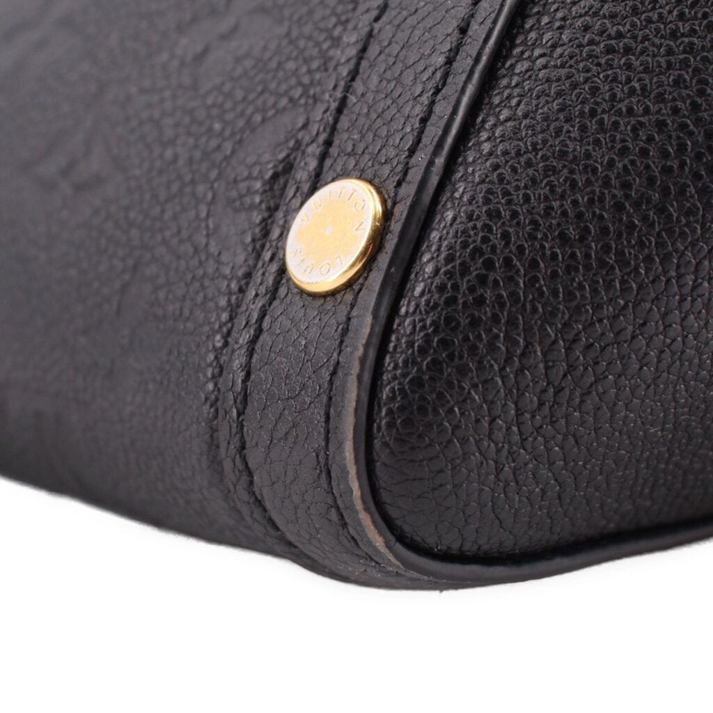 Black bag corner close-up with round gold rivet and curved seam at edge.