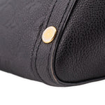 Black bag corner close-up with round gold rivet and curved seam at edge.