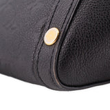 Black bag corner close-up with round gold rivet and curved seam at edge.