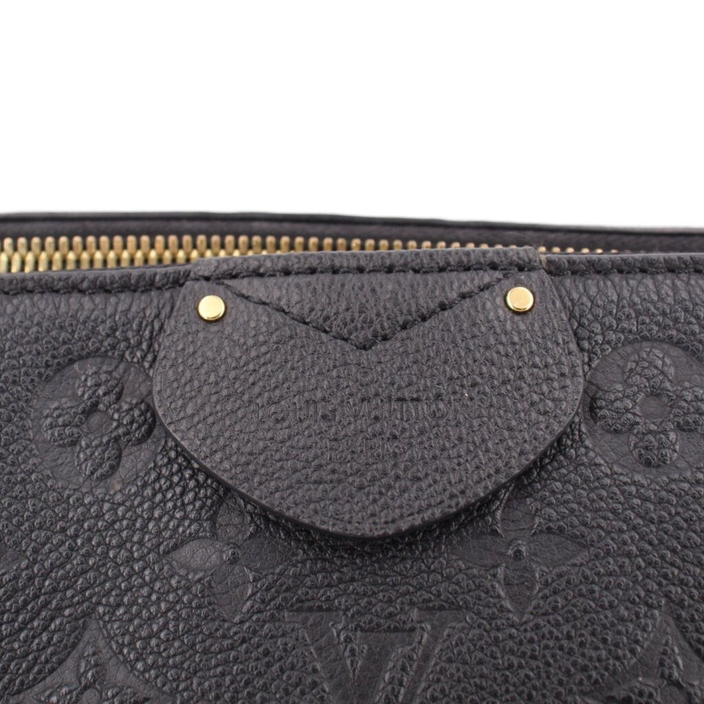 Black monogram bag close-up with curved front pouch, gold snap details, and zipper top.