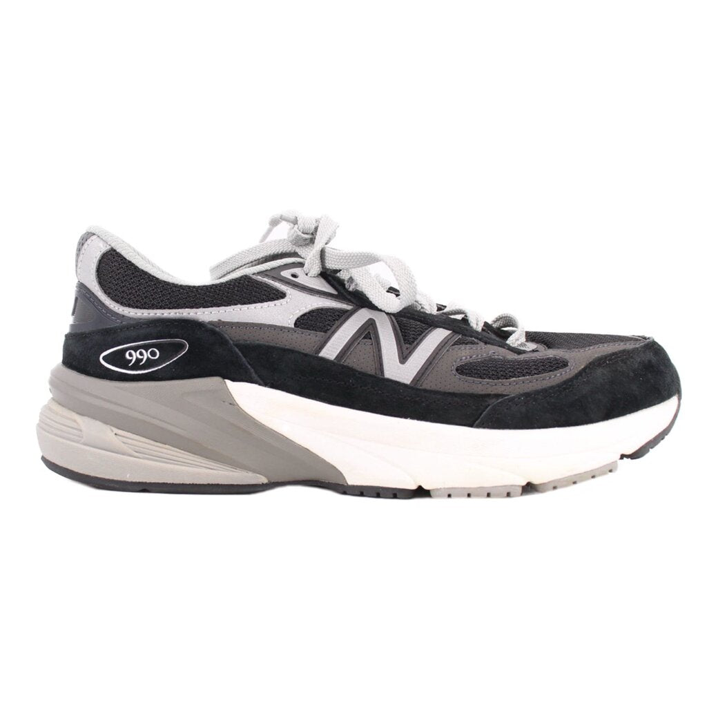 New Balance sneaker side view with black suede, gray mesh panels, and a thick cushioned sole