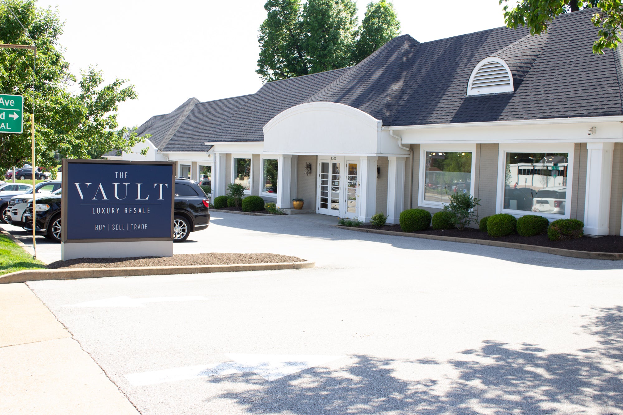 A photograph of the front of our showroom, with a navy sign reading "The Vault Luxury Resale: Buy | Sell | Trade" to the left-hand side.