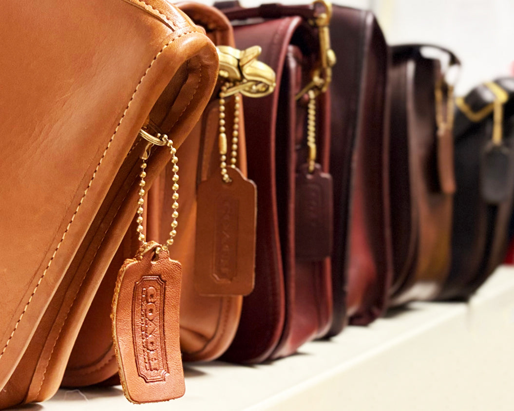 Vintage Coach handbags lined up in a gradient from a warm cognac to a dark brown color.