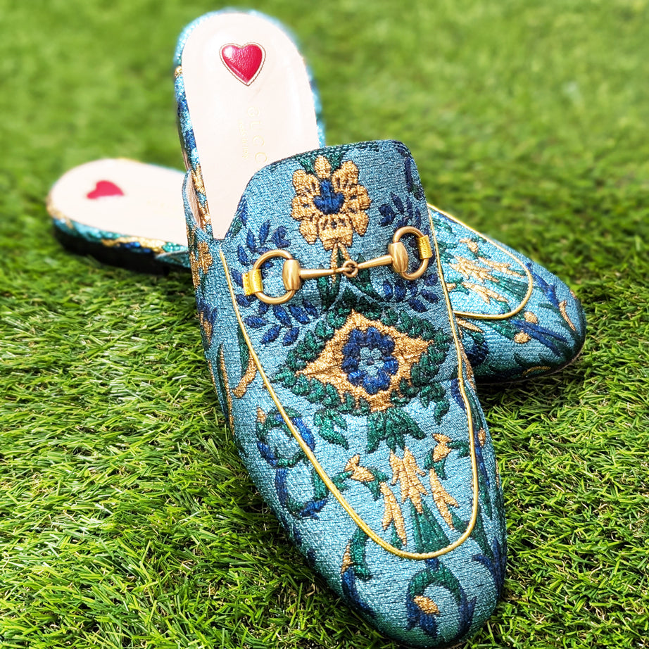 A pair of blue brocade Gucci horsebit loafers on grass.