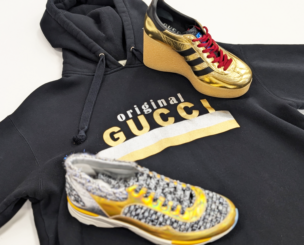 A photo of two designer shoes on top of a black Gucci hoodie.